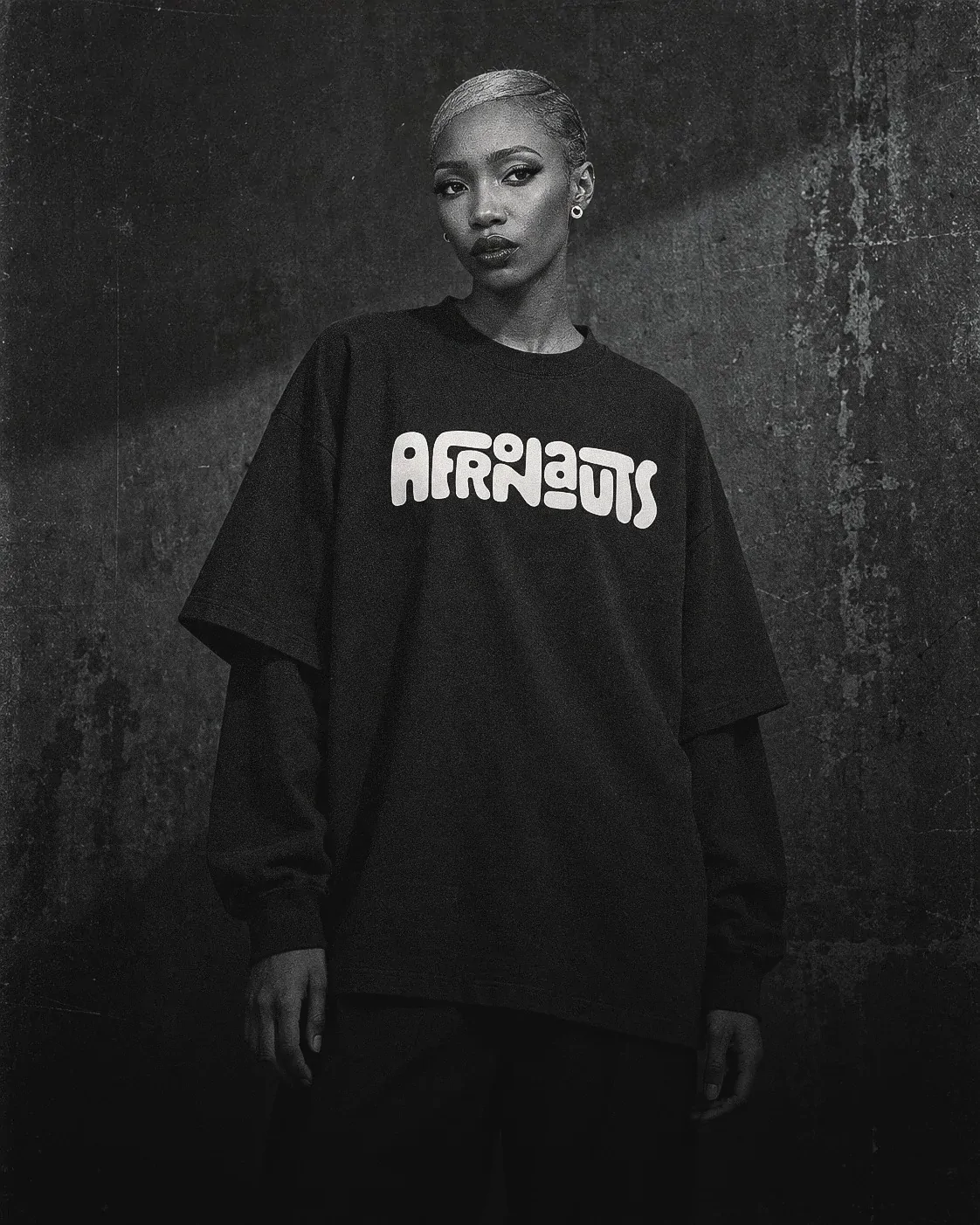 A model in the black Afronauts Layered Long-Sleeve Tee against a weathered concrete wall, in black and white.