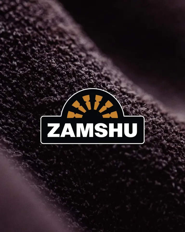 The refreshed ZAMSHU logo, with a white keyline, over a close-up of dark suede.