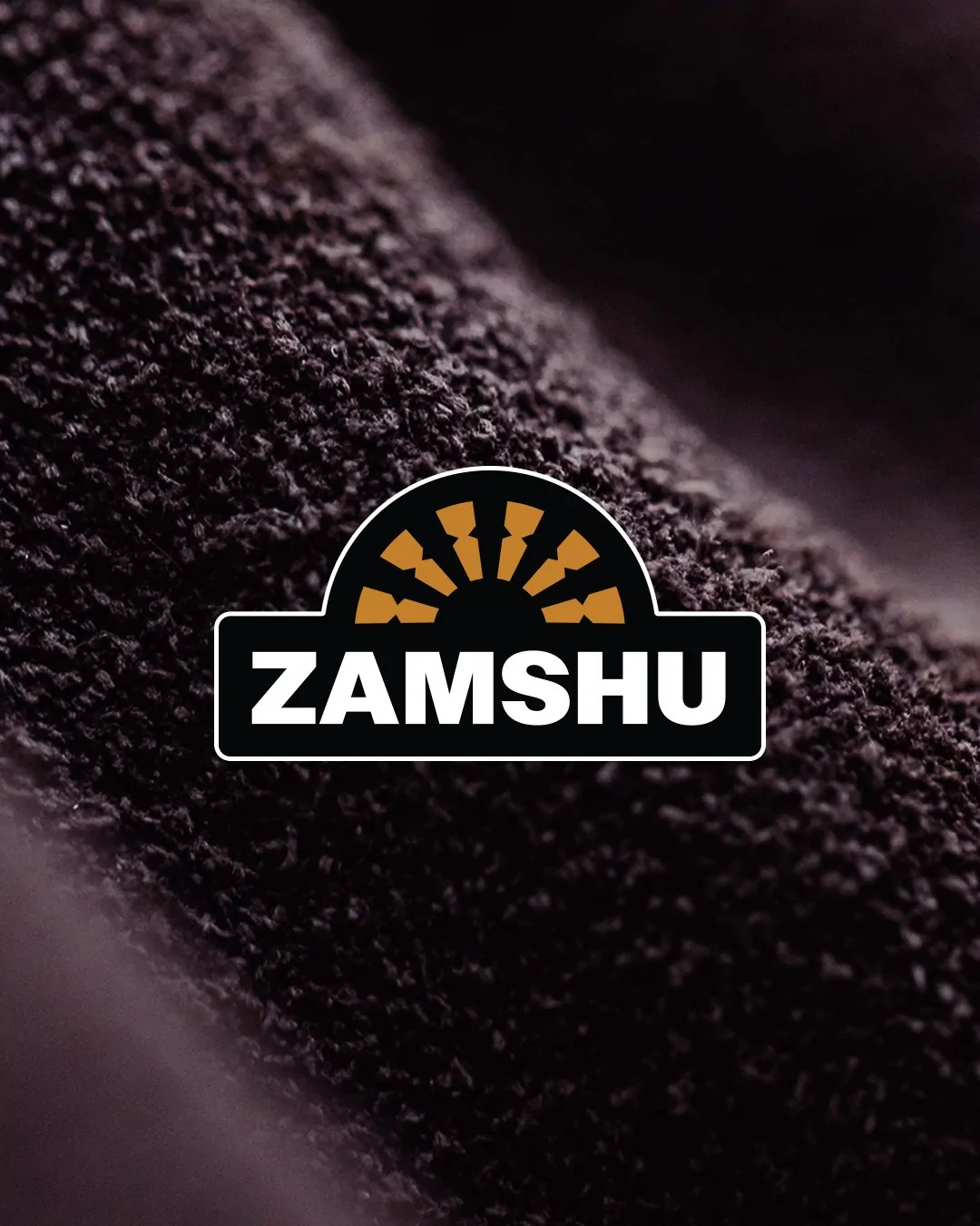 The refreshed ZAMSHU logo, with a white keyline, over a close-up of dark suede.