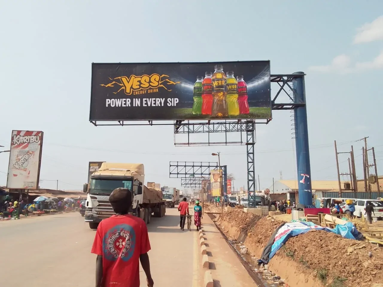A YESS Power in every sip billboard on a roadside gantry, with a boy walking along the road below.