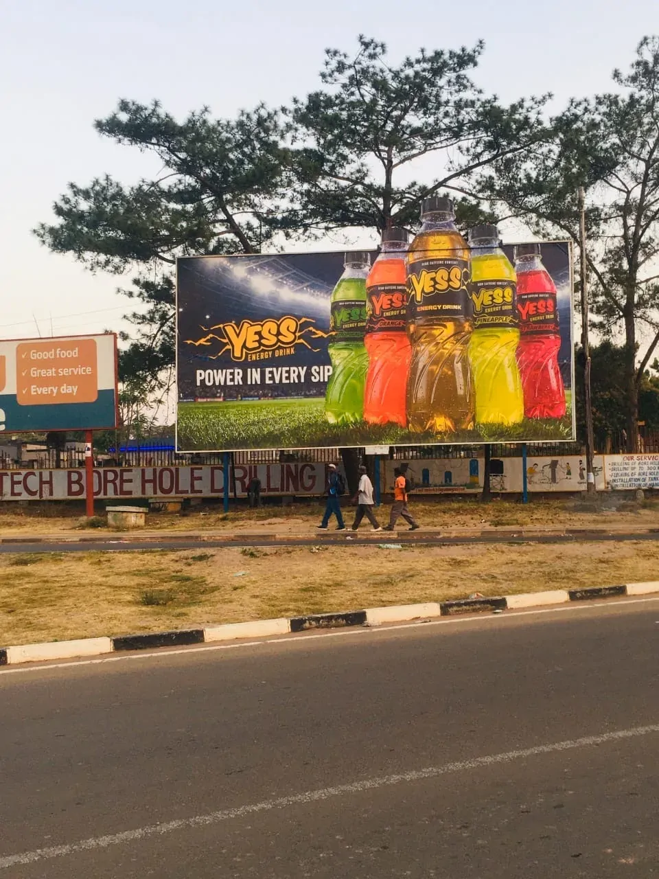 A YESS billboard on a street corner with pedestrians passing below.