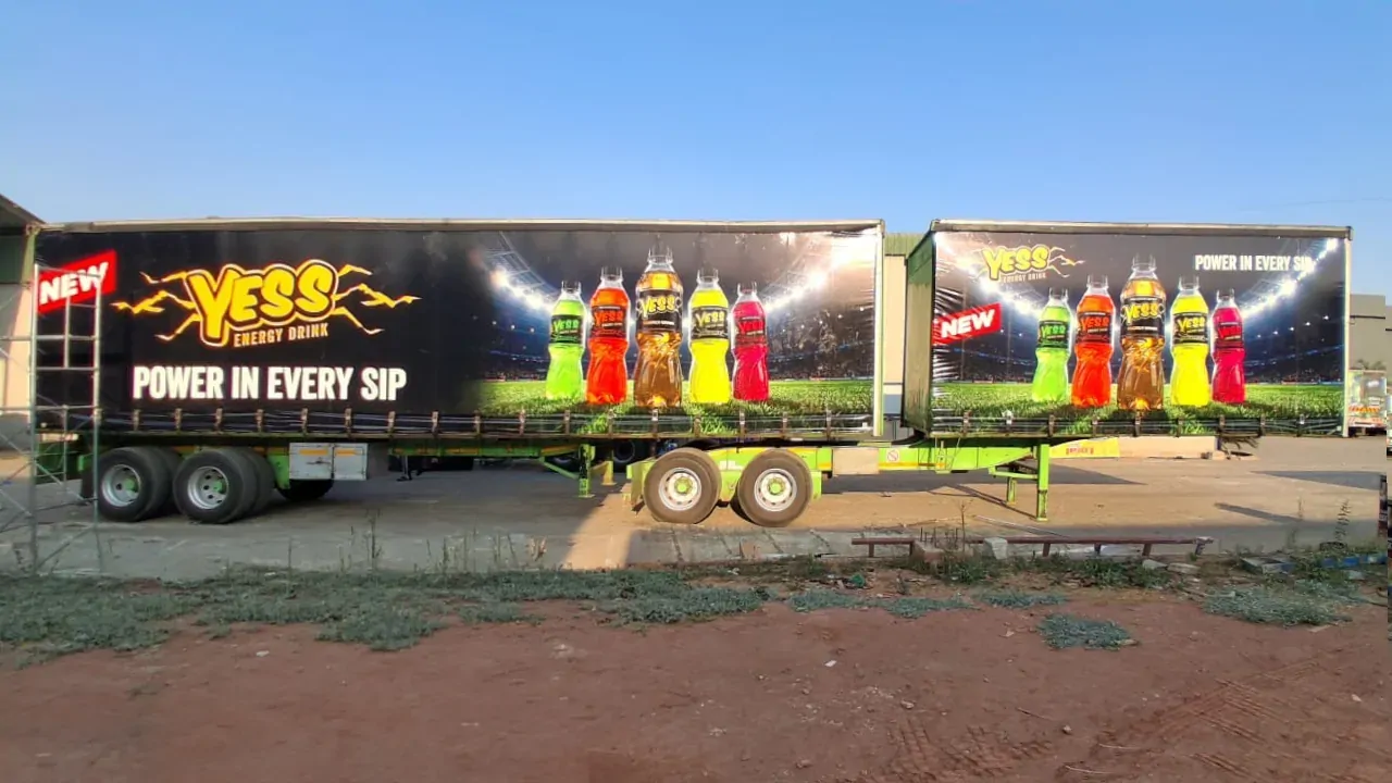 Truck trailer wrapped in YESS livery on open ground.